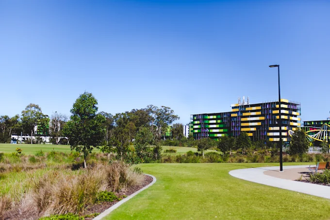 Open green parkland and a curving walking path at Village Heart with precinct buildings beyond